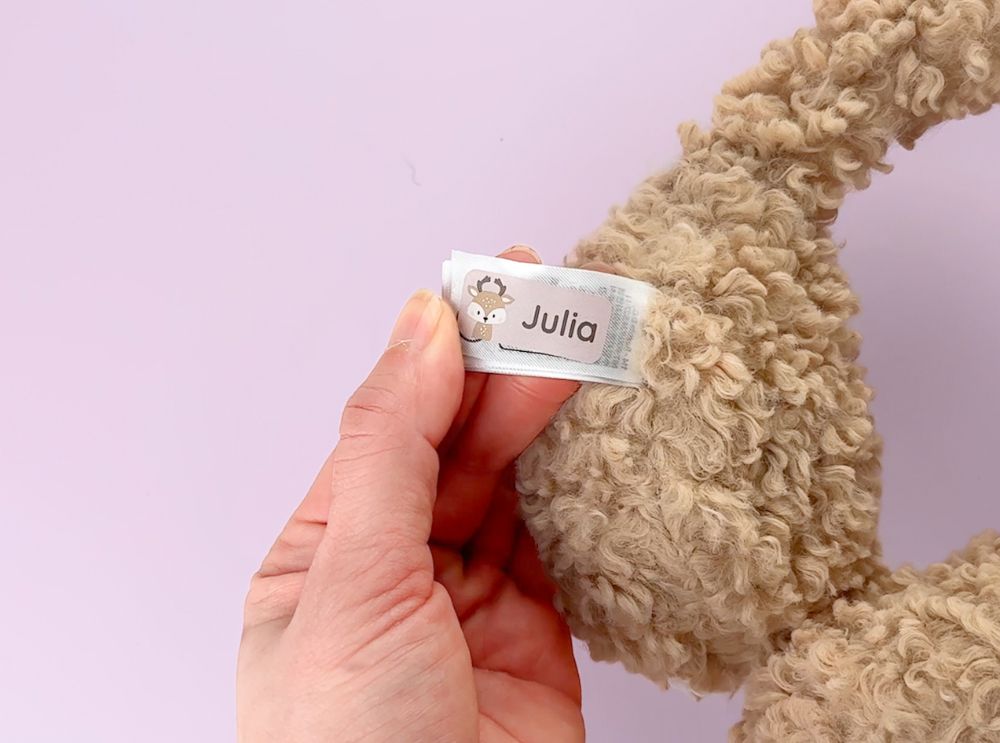 Hand holding a name label with a baby deer design, attached to a warm winter ear cover