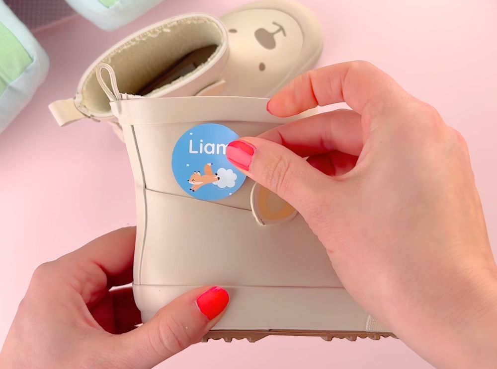 Applying a round blue name label with a fox design to a beige children's boot